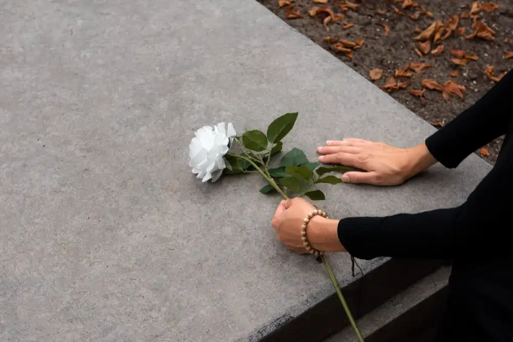 donna posa fiore bianco su lapide di marmo grigia