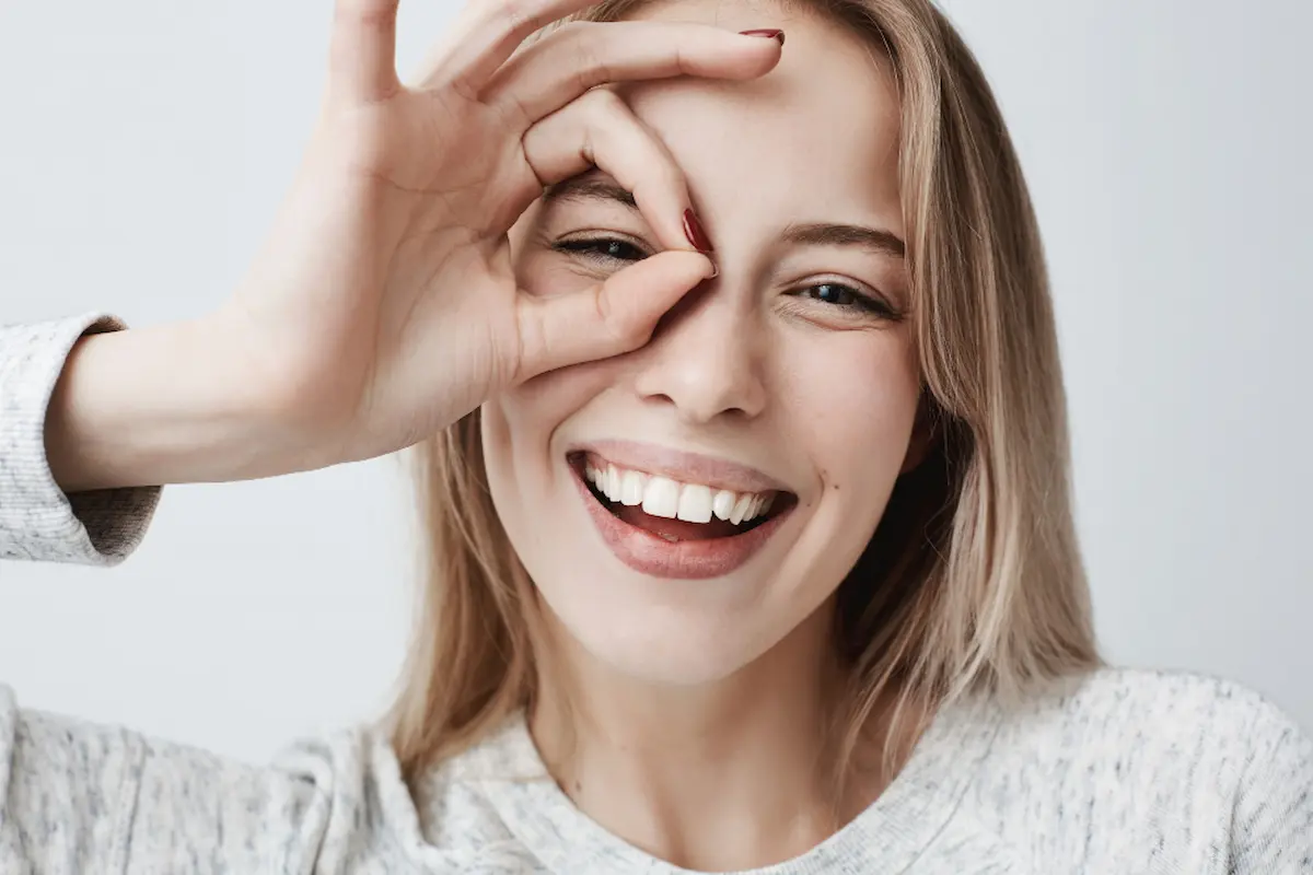 bionda sorride mostrando denti con ok su occhio