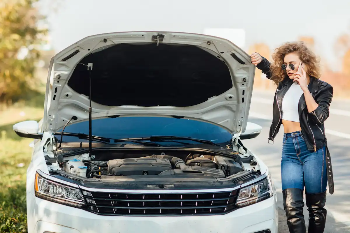 donna appoggiata a cofano dell'auto aperto
