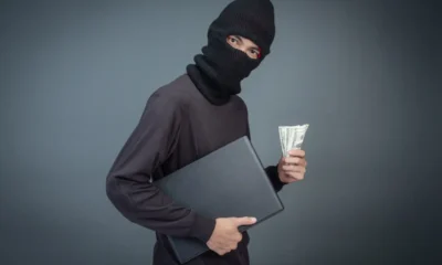 ladro con passamontagna con in mano soldi e pc