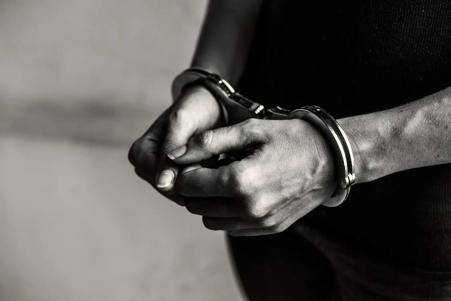 mani di uomo con manette in bianco e nero