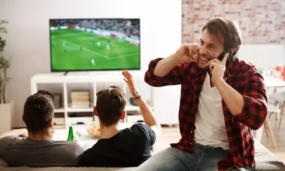 ragazzo telefona mentre amici guardano calcio in tv