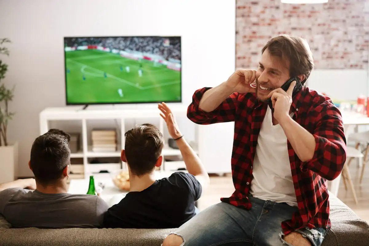 ragazzo telefona mentre amici guardano calcio in tv