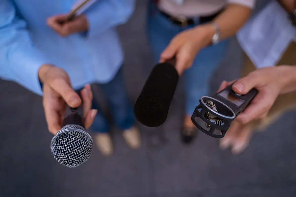 tre giornalisti tendono microfoni per intervistare