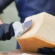 uomo taglia una forma di parmigiano