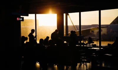 Pasajeros sentados en una terminal mientras esperan información sobre si può chiedere un pasto durante un lungo ritardo aereo.