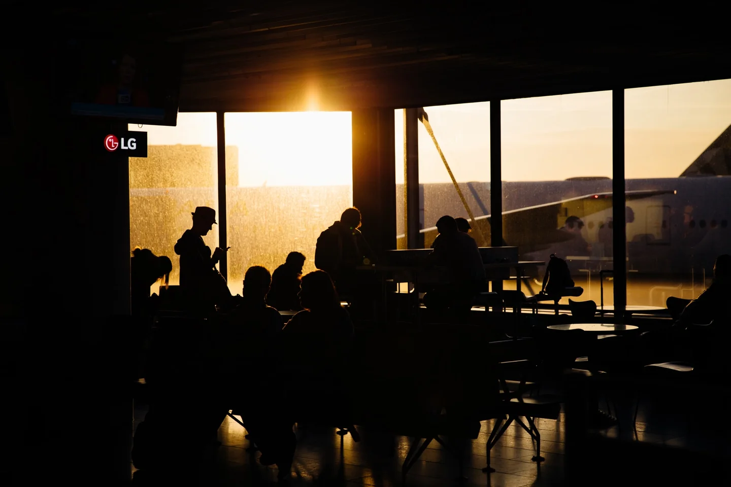 Pasajeros sentados en una terminal mientras esperan información sobre si può chiedere un pasto durante un lungo ritardo aereo.