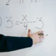 Profesor explicando come si calcola l'area del quadrato en una pizarra con fórmulas geométricas