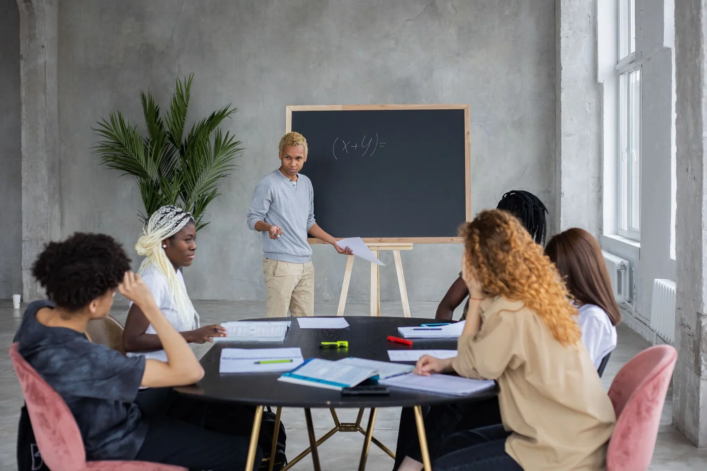 Profesor explicando come si calcola il minimo comune multiplo en una pizarra durante una clase de matemáticas.