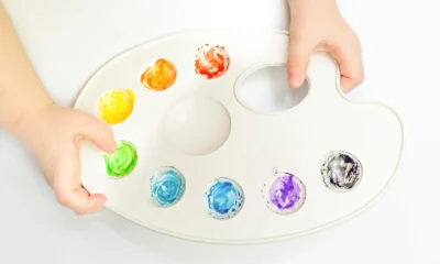 Mano mezclando pintura en una paleta para ilustrar verde e blu che colore esce en un contexto de color y pigmentos.